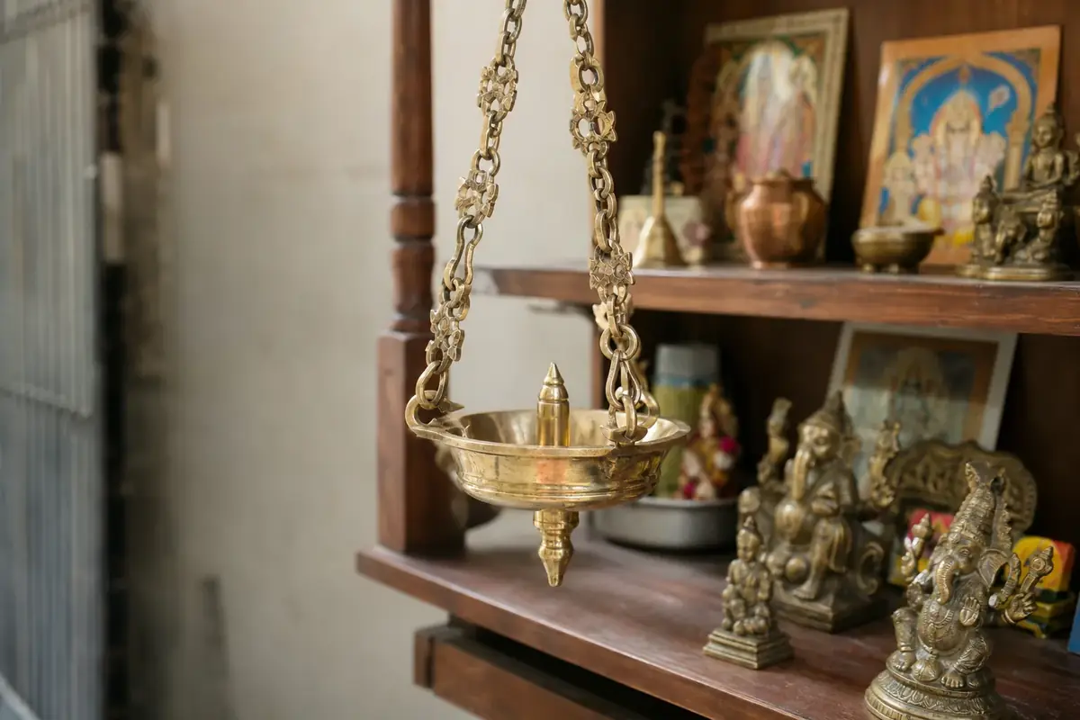 Brass hanging diya suspended near a home mandir shelf